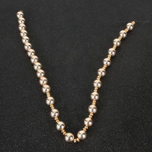 Detail view of smooth light gold beads and small gold spacers on a textured black backdrop