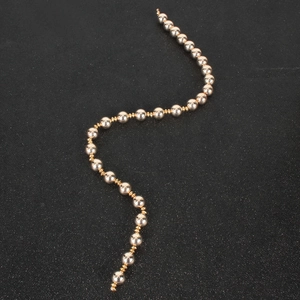 Detail of a gold beaded hair rope chain with smooth metallic spheres on a starry dark background