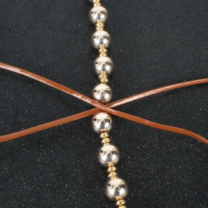 Detail of polished silver and gold beads with brown leather cords on dark fabric