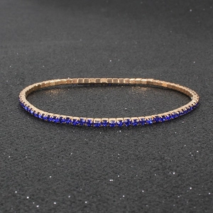 Detail of rose gold elastic bracelet with square dark blue rhinestones on dark background