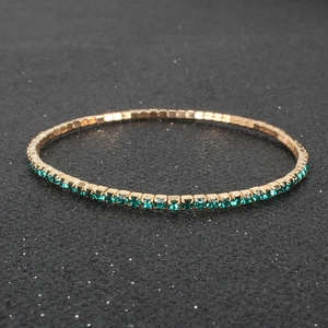 Close-up of flexible gold tennis bracelet with emerald green rhinestones on dark base