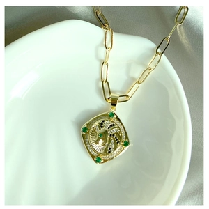 Détail d'un pendentif losange doré avec pierres vertes sur un plateau coquillage