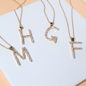 Detail view of gold-plated necklaces with M H G F pendants featuring baguette-cut zircons