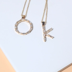 Gold plated initial necklaces O and K with cubic zirconia inlay on white stone pedestal