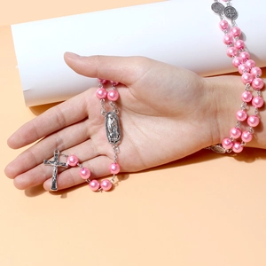 Close-up of pink pearl rosary necklace featuring a silver cross and religious medals