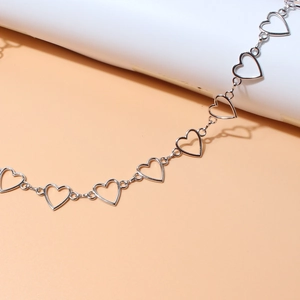 Close-up of silver hollow heart chain links with a polished mirror finish on a pink base