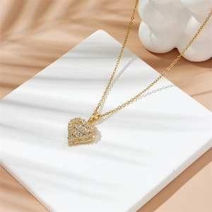 Collier cœur doré avec pendentif en zircone sur socle blanc et ombres de palmier