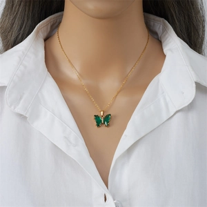 Elegante collar de mariposa dorado con cristales verde esmeralda en camisa blanca