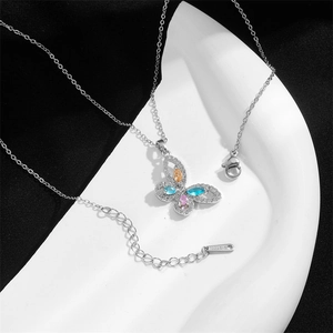 Collana in acciaio al titanio con farfalla colorata e perle su piatto di ceramica