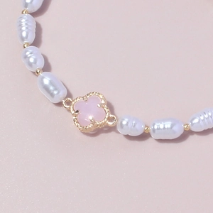 Bracciale in perle barocche con grani dorati e ciondolo quadrifoglio rosa su sfondo rosa