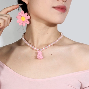 Detail der rosa Perlenkette mit Bärenanhänger und Gänseblümchen-Ohrringen an einem Modell