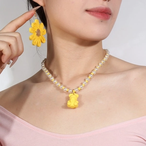 Detail der gelben Bärenkette und Sonnenblumenohrringe am Hals des Models
