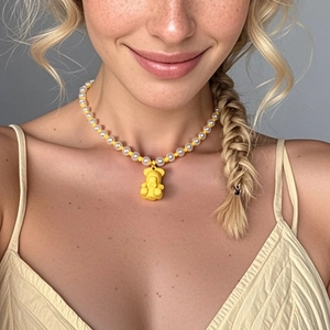 Schicke Perlenkette mit weißen Kunstperlen und gelbem Bärenanhänger an einem Modell