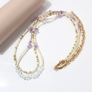 Détail d'une chaîne de taille bohème avec perles blanches, améthystes et fermoir doré