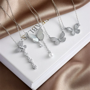 Cuatro collares de mariposa plateados con circonitas y perlas sobre fondo de seda