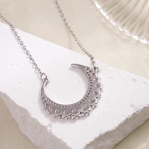 Silver crescent moon necklace with sparkling zircons on a white textured stone base