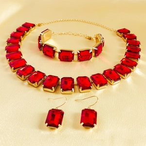 Detailed macro view of red rhinestone necklace, bracelet, and earrings set on gold fabric