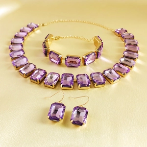 Detail of elegant gold-tone jewelry set with rectangular purple gemstones on silk