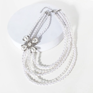 Détail d'un collier de perles multicouche avec un pendentif floral et strass brillants