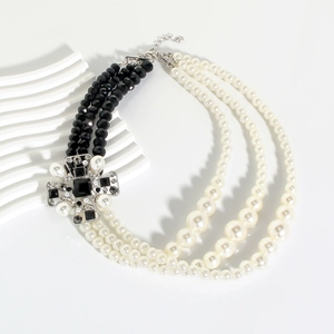 Detail of multi-layer pearl necklace featuring a large vintage cross pendant with black gems