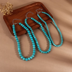 Three minimalist turquoise beaded necklaces with silver clasps on a warm wooden tray