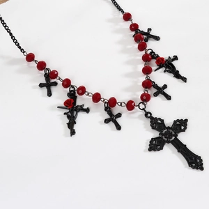 Macro view of gothic black cross necklace with red beads and rose details on white background