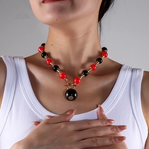Détail du collier de perles rouges et noires avec pendentif fleur dorée et fermoir à bascule