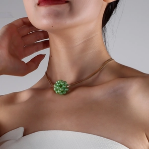 Detail einer goldenen Schlangenkette mit grünem Perlenanhänger für einen eleganten Look