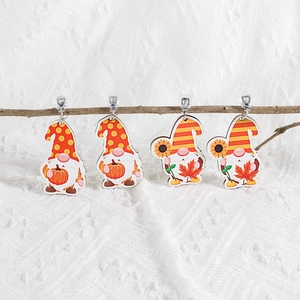 Close-up of wooden gnome earrings with pumpkin and maple leaf designs on a branch