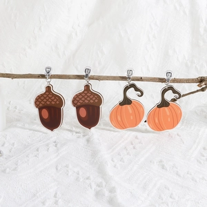 Detail of wooden pumpkin and acorn earrings hanging on a branch for Thanksgiving