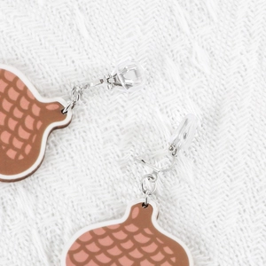 Macro detail of wooden clip-on earrings with pink and brown scale pattern on white knit