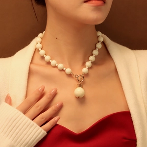Détail du collier de perles blanches avec fermoir à bascule doré et pendentif boule sur modèle