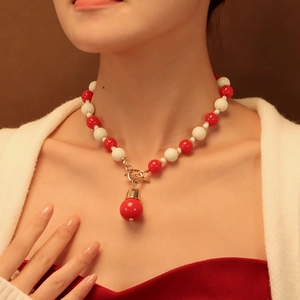 Détail du collier avec perles rouges et blanches et fermoir en T en métal doré sur modèle
