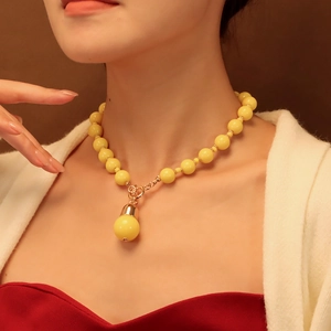 Détail d'un collier de perles jaunes avec pendentif goutte porté par un mannequin