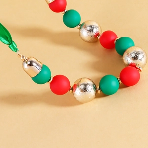 Detail of Christmas necklace with red and green beads, golden bell, and silk ribbon