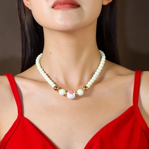 Détail du collier de perles avec un motif flocon rouge sur perle blanche et accents dorés