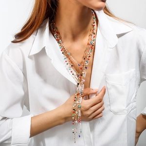 Dettaglio di collane dorate a strati con perline colorate e bianche su camicia bianca
