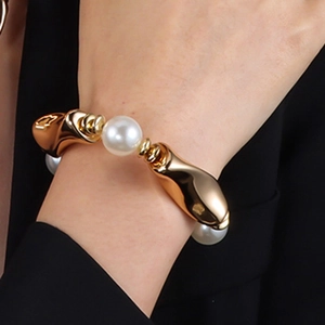Nahaufnahme eines klobigen goldenen Metallarmbands mit weißen Perlen am Handgelenk