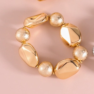 Nahaufnahme des goldenen elastischen Perlenarmbands mit glatten und gehämmerten Texturen