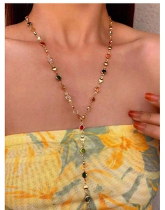 Dettaglio di una collana a Y dorata con cristalli multicolore su una modella donna