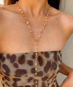 Primo piano di una collana a Y dorata con cristalli trasparenti indossata da una modella