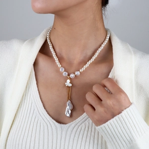 Détail d'un collier de perles élégant avec pendentif papillon porté sur un pull blanc