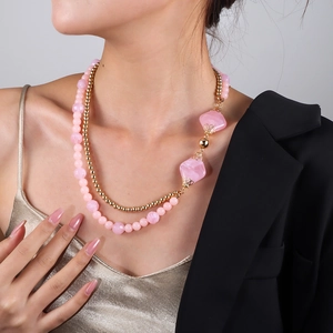 Detail einer geschichteten Goldperlenkette mit rosa geometrischen Perlen am Model