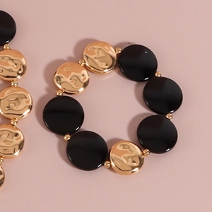 Detail von goldenen gehämmerten Metallscheiben und schwarzen runden Perlen am Armband