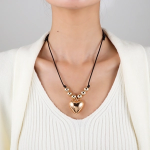 Détail d'un pendentif cœur doré et de perles métalliques sur un collier cordon noir