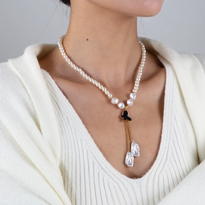Détail d'un collier de perles élégant avec pendentif papillon noir et pompons dorés