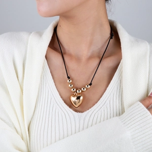 Détail d'un pendentif cœur doré sur un cordon noir ajustable porté par un mannequin