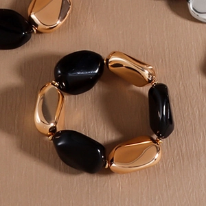 Makro-Detail des elastischen Armbands mit kontrastierenden schwarzen und goldenen Perlen