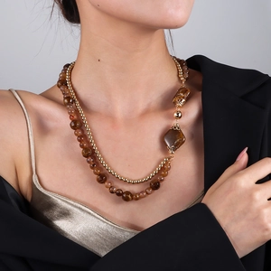 Detail einer mehrlagigen goldenen Perlenkette mit Marmorperlen und geometrischem Anhänger