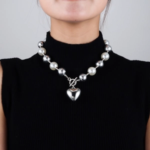 Détail d'un collier de perles blanches, boules argentées et pendentif cœur sur mannequin